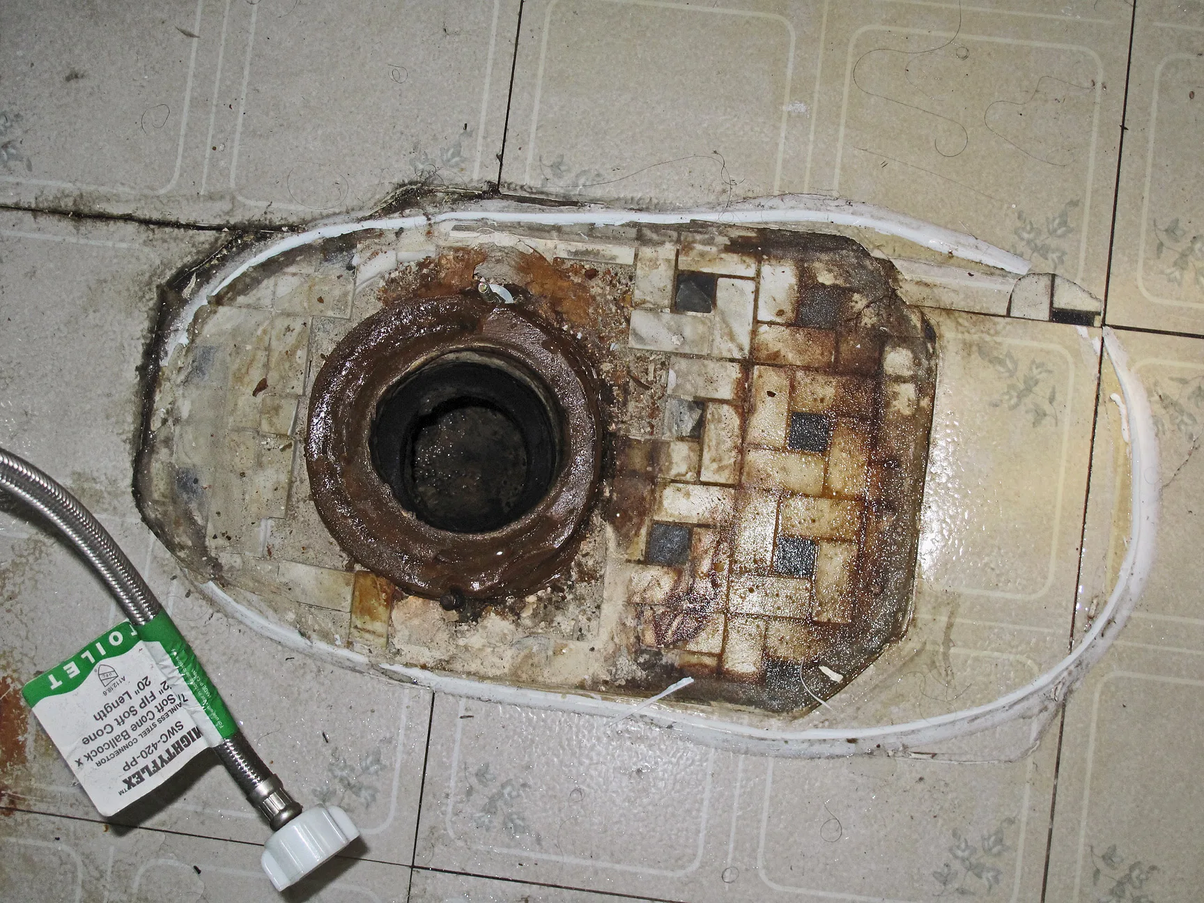 Drain hole in bathroom floor before installation of new toilet. The original tiled floor (1920s apartment building, Los Angeles, California) is visible underneath the linoleum. The hose for the water supply to the toilet is also visible. What makes an accessible renovation bigger than it looks